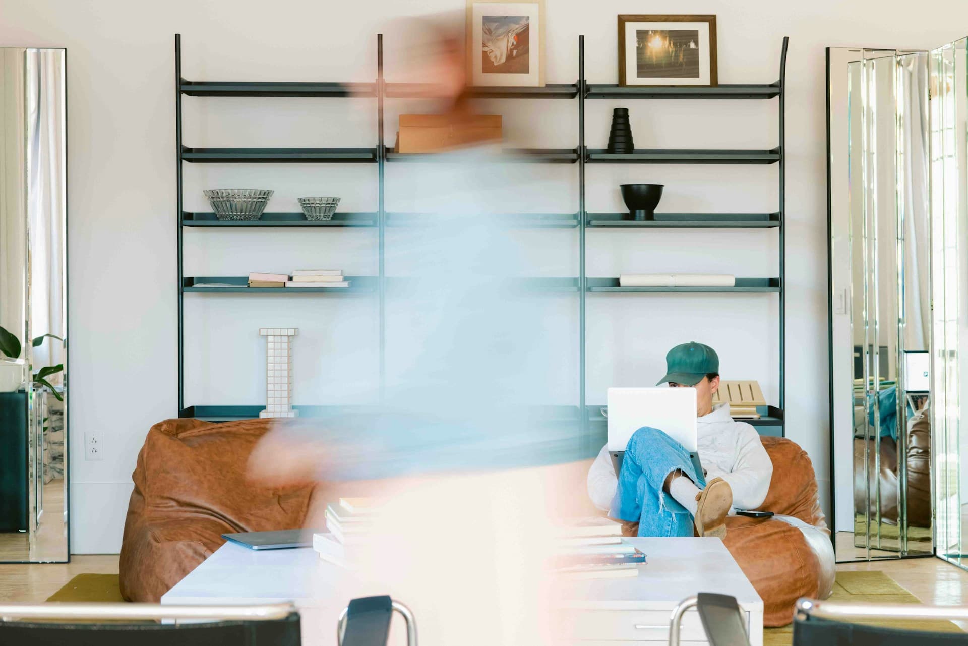A photo of a person sitting on a couch with another person walking in front of the camera